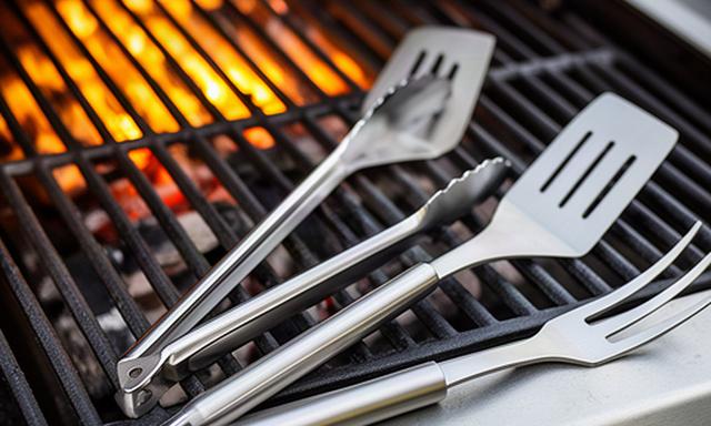 Dreiteiliges Grillbesteck aus Edelstahl neben einem heissen Grillrost